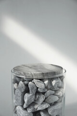 Presentation for product. Glass container with stones on light grey background. Space for text