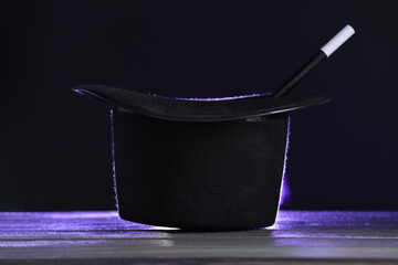 Magician's hat and wand on wooden table against black background