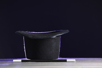 Magician's hat and wand on white wooden table against black background