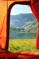 View from inside a orange tourist tent to mountains and lake. Beautiful Summer landscape. freedom, adventure, privacy, unity with wild nature, tourism and travel concept. Camping place