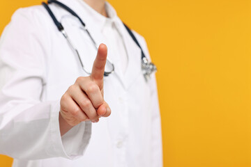 Doctor with stethoscope pointing on orange background, closeup. Space for text