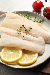 Plate with raw cod fish, spices, microgreens and lemon on grey table, closeup