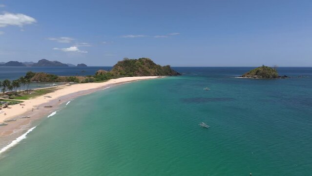 Aerial panning shot over twin beach north of El Nido with palm trees lining the shore.