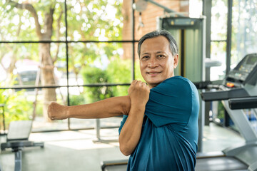 Senior asian man wearing sportswear warming up in fitness gym before exercise. Mature man...