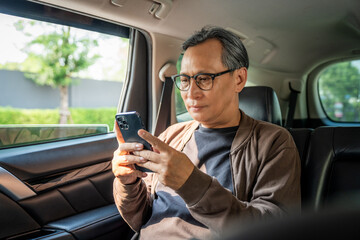 Relaxing moment of mature man sitting in car back seats using smartphone application on social media look out the window. Senior man happy in car traveling on the road to destination.