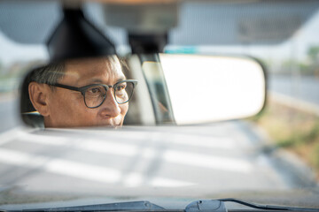 Rear view mirror. Close up shot eye of senior asian man looking roadway while driving car in the morning. Mature Man sitting in car.