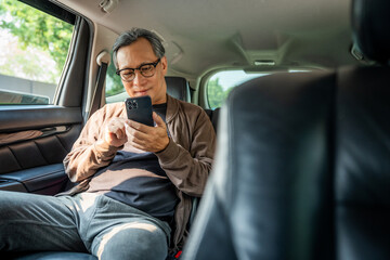 Relaxing moment of mature man sitting in car back seats using smartphone application on social...