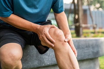 Mature man tired and leg pain during jogging at nature park. Runner has sore knees because he has...