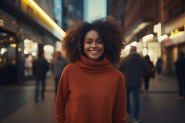 Portrait of a grinning afro-american woman in her 30s dressed in a comfy fleece pullover isolated on bustling city street at night
