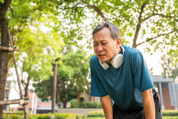 Senior asian man tired during jogging at outdoor nature park. Mature asian male intense training workout challenge breathing exhausted. Healthy and activity lifestyle concept.