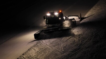 Snow groomer working at night in the Dolomites, Italian Alps, with bright lights and a clear trail behind