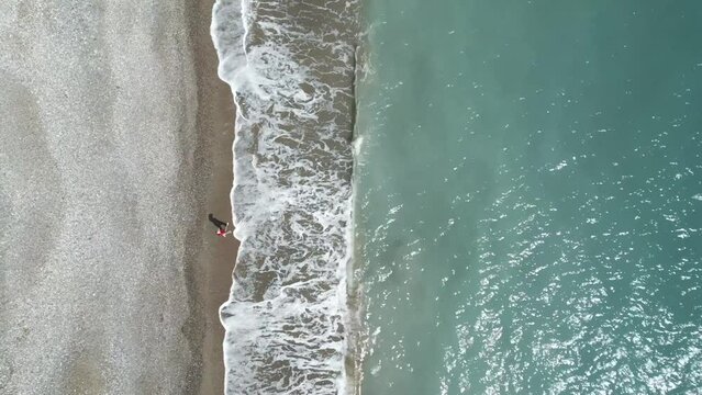 A lone person walking on pissouri beach in cyprus, waves gently crashing, aerial view