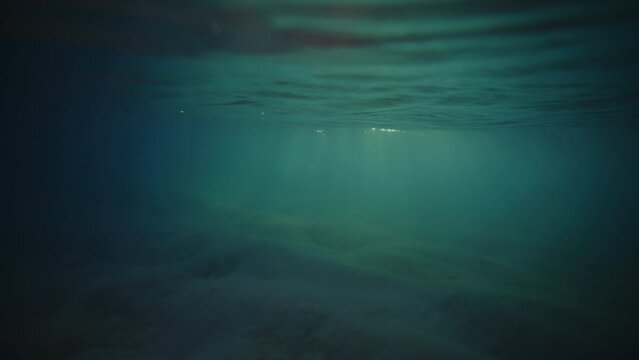 Underwater view of mystic turquoise green rays of light on sandy water