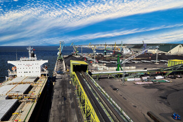 Coal Harbor and maritime bulk terminal with port cranes, coal embankments, bulk carriers at berth.