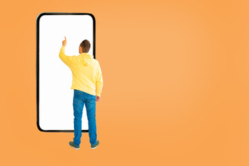 Rear view of boy pointing at smartphone screen against orange background.