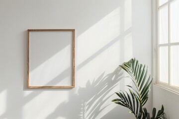 Wooden picture frame hanging on a white wall next to a potted plant, creating a clean and simple aesthetic
