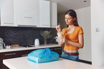 Woman standing in kitchen with plastic bag in hand, preparing food and organizing groceries