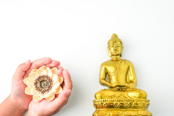A child holding and offering white lotus flower in the palm of hands next to Golden statue of a...