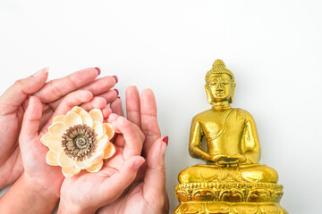 Mom and child holding and offering white lotus flower in the palm of hands next to Golden statue of...