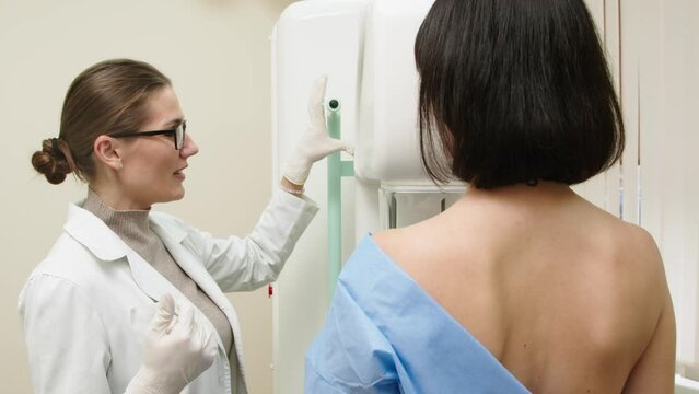 A female doctor in a modern clinic explains the mammography procedure to a topless adult patient undergoing a mammogram. A healthy woman is engaged in cancer prevention in a hospital ward.