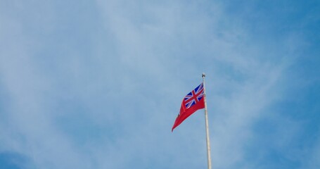 Fluttering British colony flag, vivid against blue sky, symbolizes historic pride, enduring legacy....
