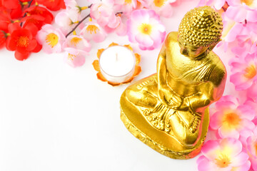A golden statue of a Buddhist figure meditating decorate with colorful flowers and round white candle isolated on white background. Concept for Vesak Day and Enlightenment Day