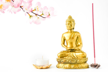 A golden statue of a Buddhist figure meditating decorate with colorful flowers, round white candle and red colored incense isolated on white background. Concept for Vesak Day and Enlightenment Day