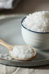Organic salt in bowl and wooden spoon on table, closeup