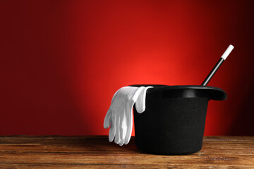 Magician's hat, gloves and wand on wooden table against red background, space for text