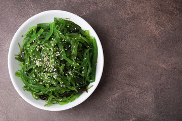 Tasty seaweed salad in bowl on brown table, top view. Space for text