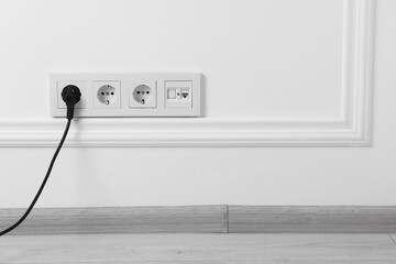 Power sockets and electric plug on white wall, space for text