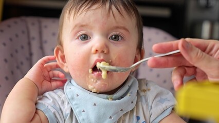 dirty baby eats porridge from a spoon. our dirty baby loves porridge and mess. happy family kindergarten kids concept. baby loves to eat porridge for breakfast. close-up baby dream eating porridge