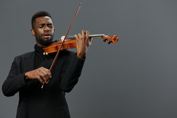 Elegant African American Man in Black Suit Playing Violin on Gray Background in Studio Setting - obrazy, fototapety, plakaty