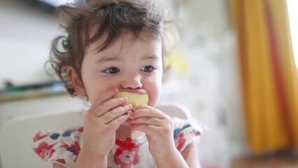 girl eats an apple. happy family child dream concept. little girl stands indoors and eats half an...