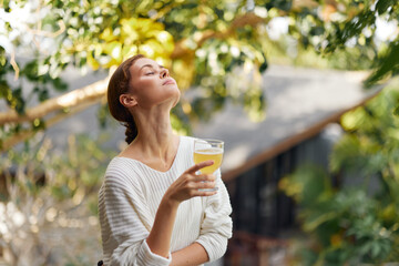 Relaxing with a Glass of Refreshing Kombucha, Surrounded by Nature's Beauty Happy woman enjoys a...