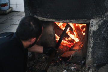 male cook lights a wood-burning stove for big cauldron for cooking Uzbek pilaf in oriental kitchen...