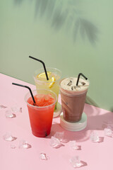 Three takeaway glasses of summer drinks with palm shadow. Lemonade on colored background