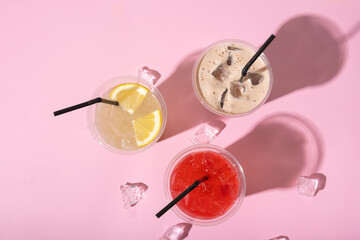 Three takeaway glasses of summer drinks with ice. Lemonades and cocktail on colored background