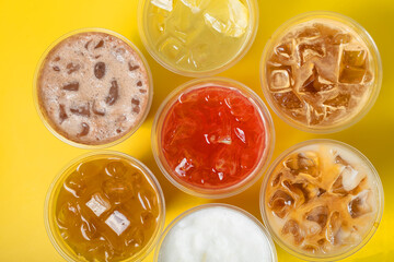 Takeaway glasses of summer drinks with ice top view. Lemonades and coctails on yellow background