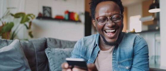 Smiling Black African American man on a sofa in living room having a video call with his friends and family on his smartphone.