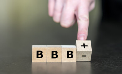 Hand turns wooden cube and changes the expression BBBminus to BBBplusplus. Symbol for a upgrade in...