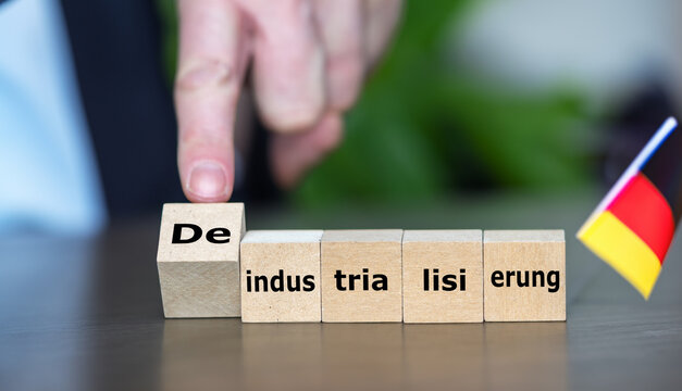 Hand turns wooden cube and changes the German expression 'Industrialisierung' (industrialization) to 'Deindustrialisierung' (deindustrialization). Symbol for a weak economy in Germany.