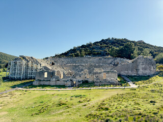 The remnants of an ancient theater in Patara, Antalya, Turkey, sit at the base of a lush hillside,...