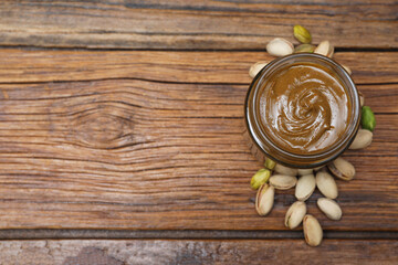 Tasty pistachio nut paste in jar on wooden table, top view. Space for text