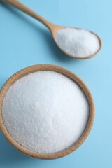 Organic white salt in bowl and spoon on light blue background, above view