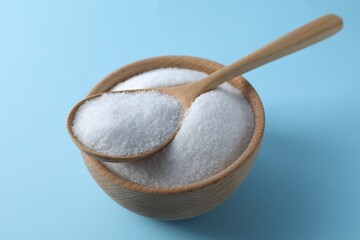 Organic white salt in bowl and spoon on light blue background, closeup