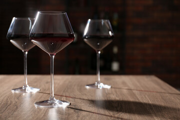Tasty red wine in glasses on wooden table, space for text