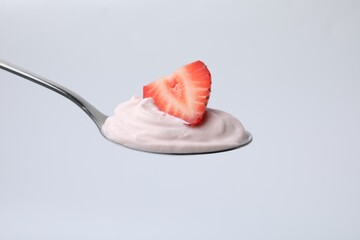 Delicious natural yogurt with fresh strawberry in spoon on light background