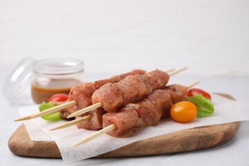 Wooden skewers with cut raw marinated meat on light grey table, closeup