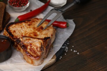 Tasty grilled meat, marinade, fork and chili on wooden table, closeup. Space for text